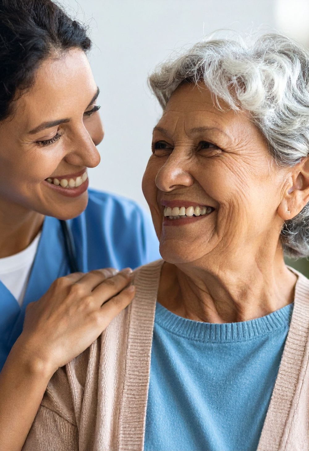 A smiling caregiver gently places a reassuring hand on a senior woman’s shoulder, sharing a warm and supportive moment during in-home care in Dublin, Ohio.