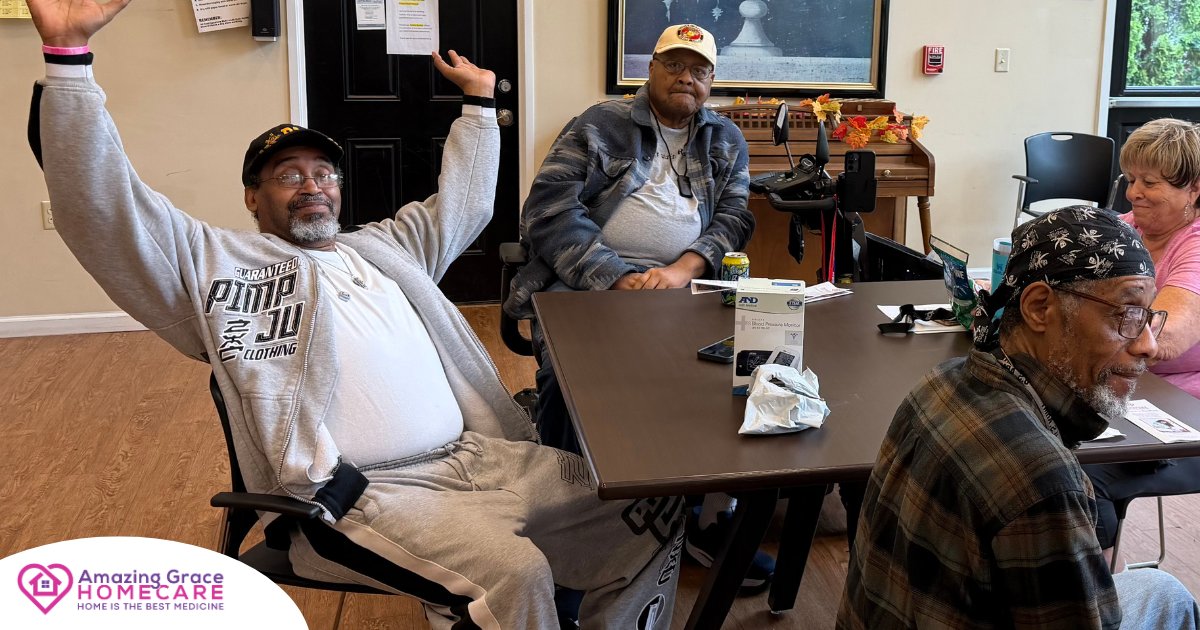 A group of seniors gathered around a table; one man joyfully raises his arms while others look on. A blood pressure monitor box sits on the table, indicating a health workshop.